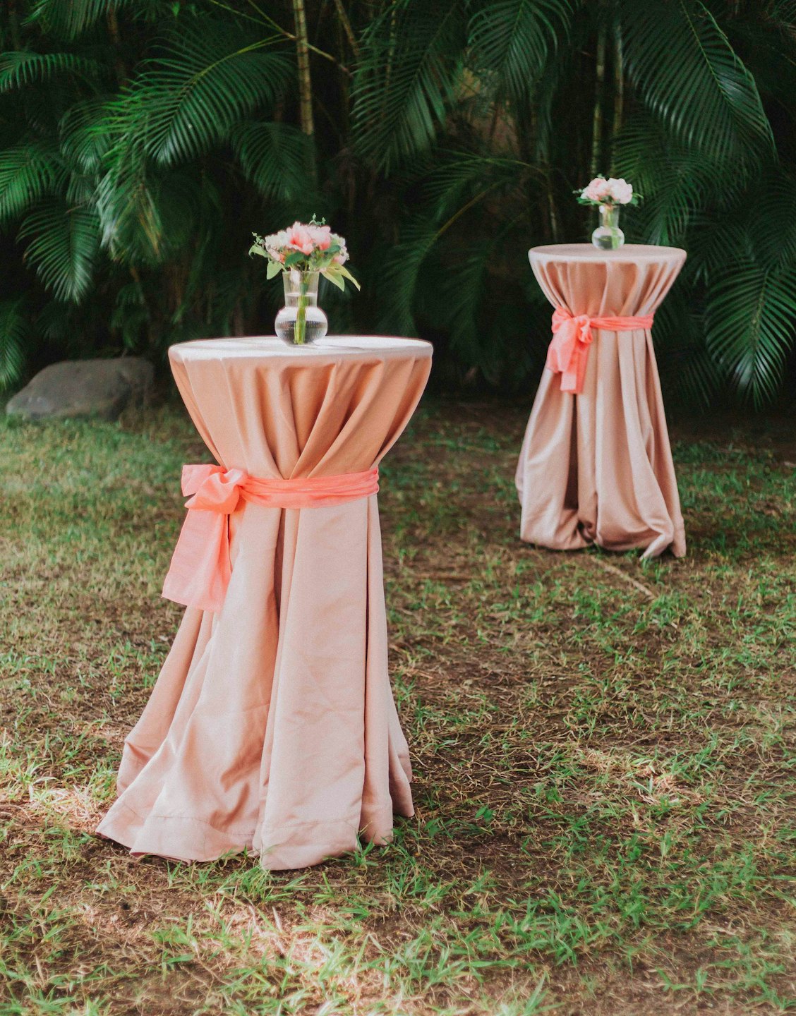 Deux tables avec des nappes pêche et des arrangements floraux sur l'herbe.