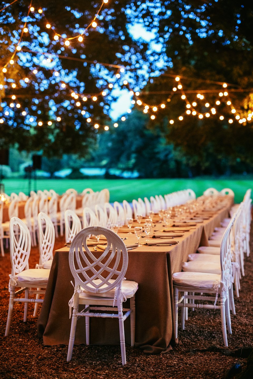 Tables à manger avec des chaises blanches disposées sur une pelouse.