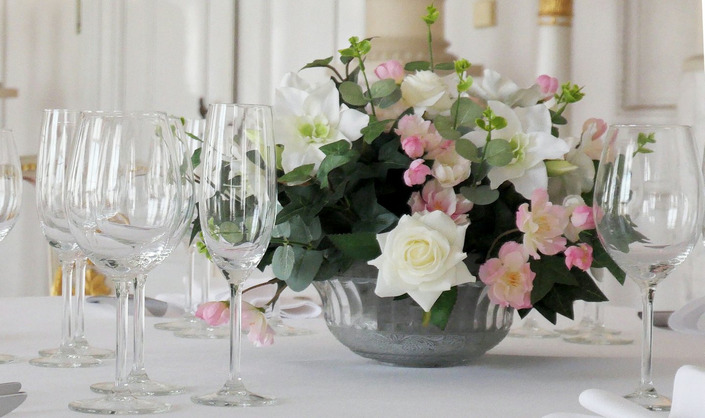 Des verres en cristal entourent un centre de table floral sur une table blanche.
