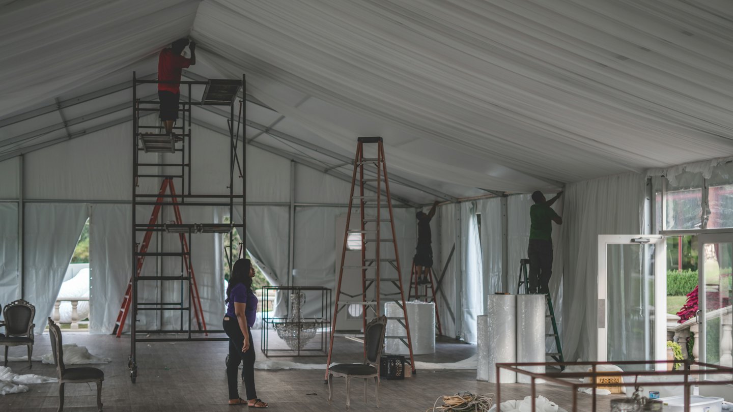 Des professionnels de l'événementiel travaillent aux décorations intérieures d'une grande tente.